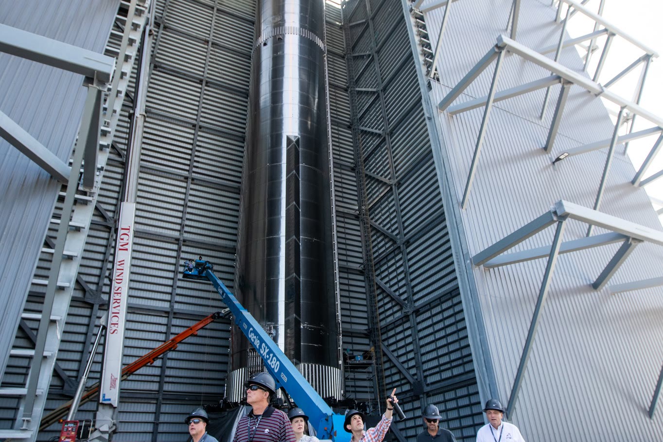 SpaceX workers looking up at the engine section of a Super Heavy booster